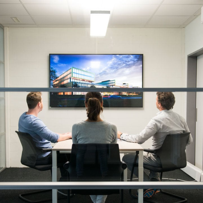 Tre persone in una sala riunioni osservano una visualizzazione digitale di un edificio moderno su un display a parete.
