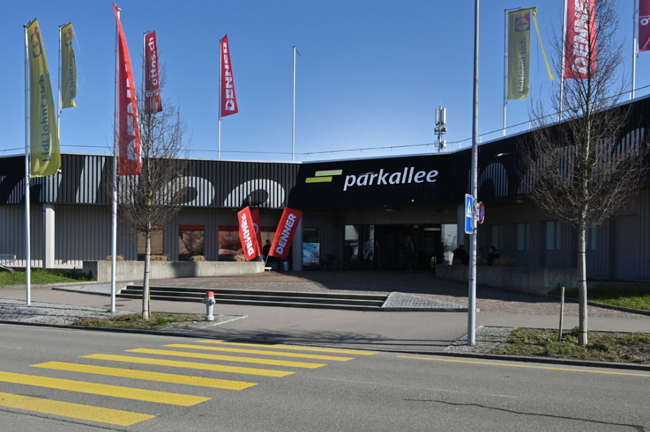 Das Einkaufszentrum Parkallee in Bachenbülach nach seiner Revitalisierung. Von Frühling 2023 bis Sommer 2024 wurde auch das zweigeschossige Parkhaus vollständig neu beleuchtet. Dies bedeutet mehr Sicherheit, ein einladendes Erscheinungsbild und deutlich weniger Energieverbrauch. Einkaufszentrum Parkallee in Bachenbülach nach der Revitalisierung, mit vollständig neu beleuchtetem zweigeschossigem Parkhaus für mehr Sicherheit, ein einladendes Erscheinungsbild und geringeren Energieverbrauch (Frühling 2023 bis Sommer 2024).